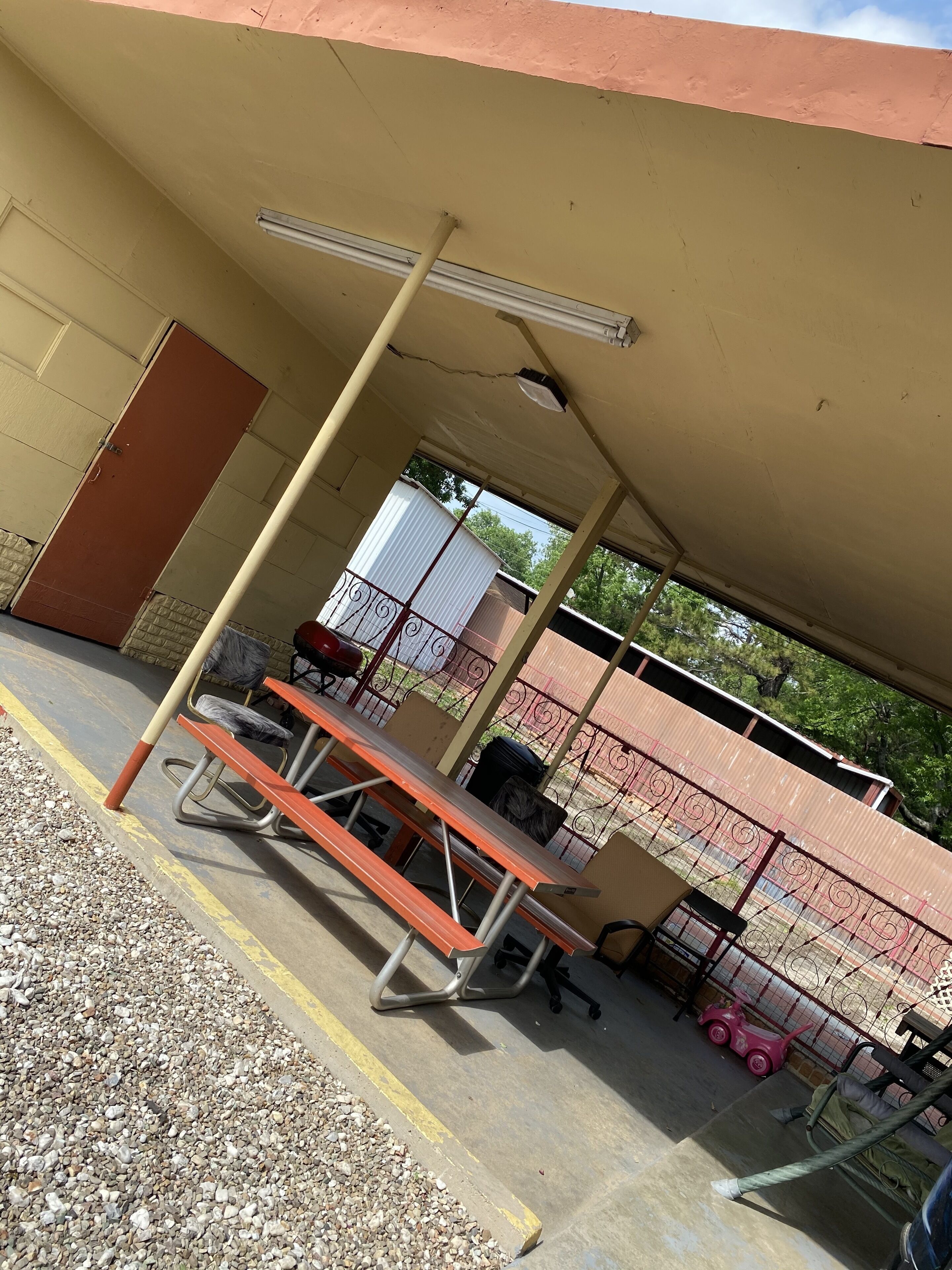 Un espacio al aire libre techado con una mesa de picnic y sillas, un basurero y una cerca.