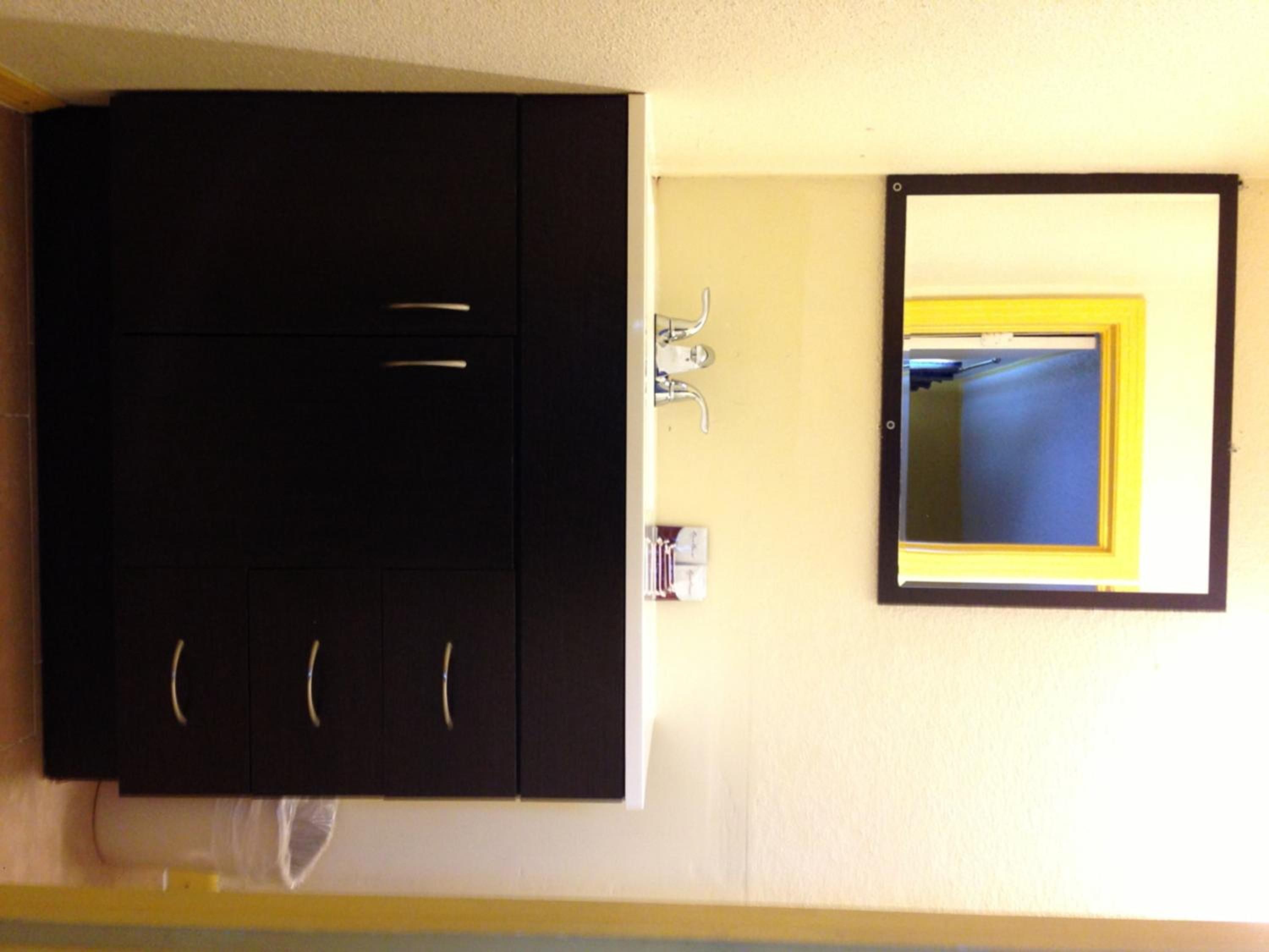 A room with a dark-colored wardrobe, a small sink with a faucet, and a mirror with a yellow frame.