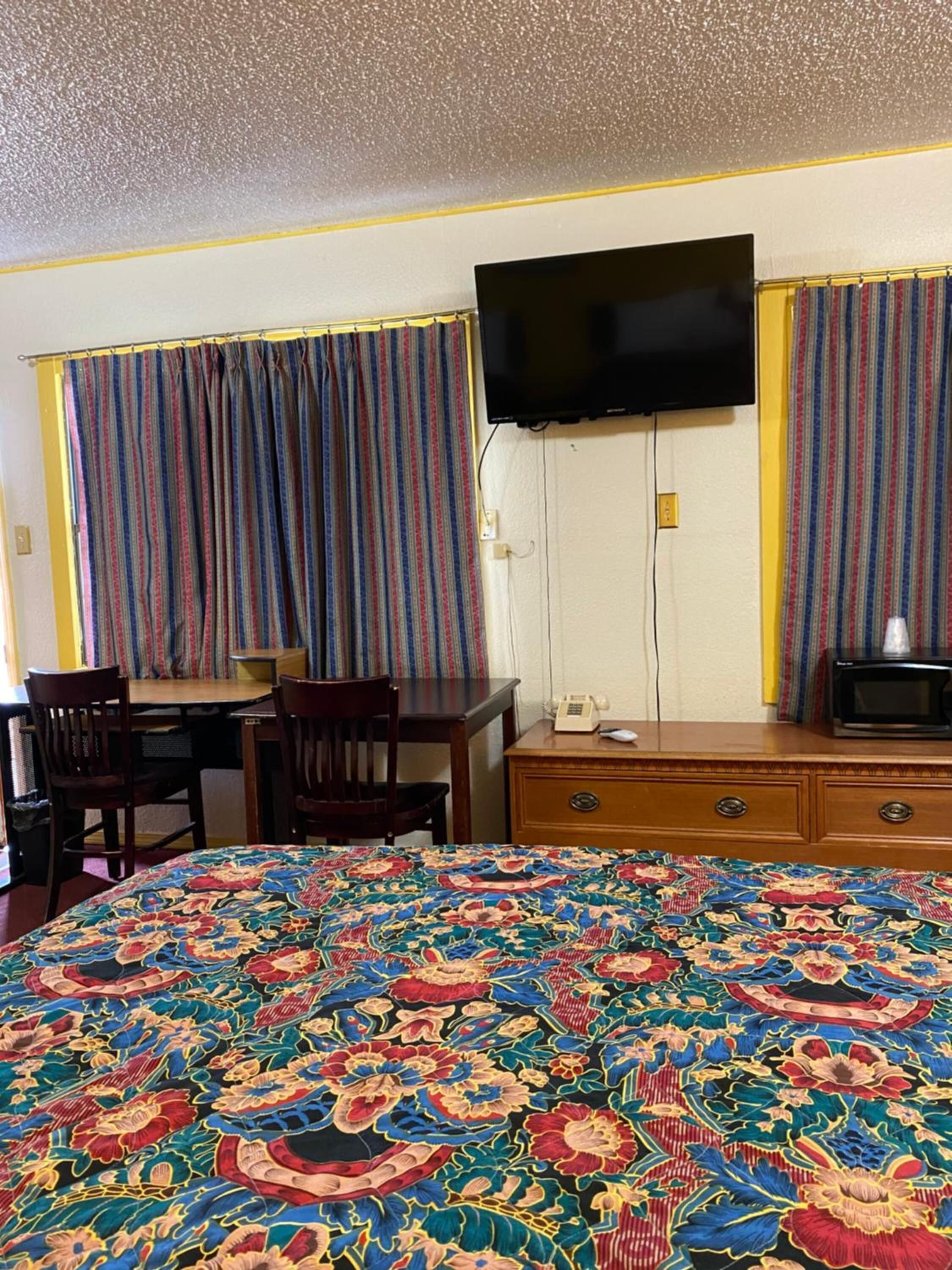 Une chambre d’hôtel avec un grand lit, un bureau, une chaise, un téléviseur fixé au mur et un four à micro-ondes posé sur une commode en bois.