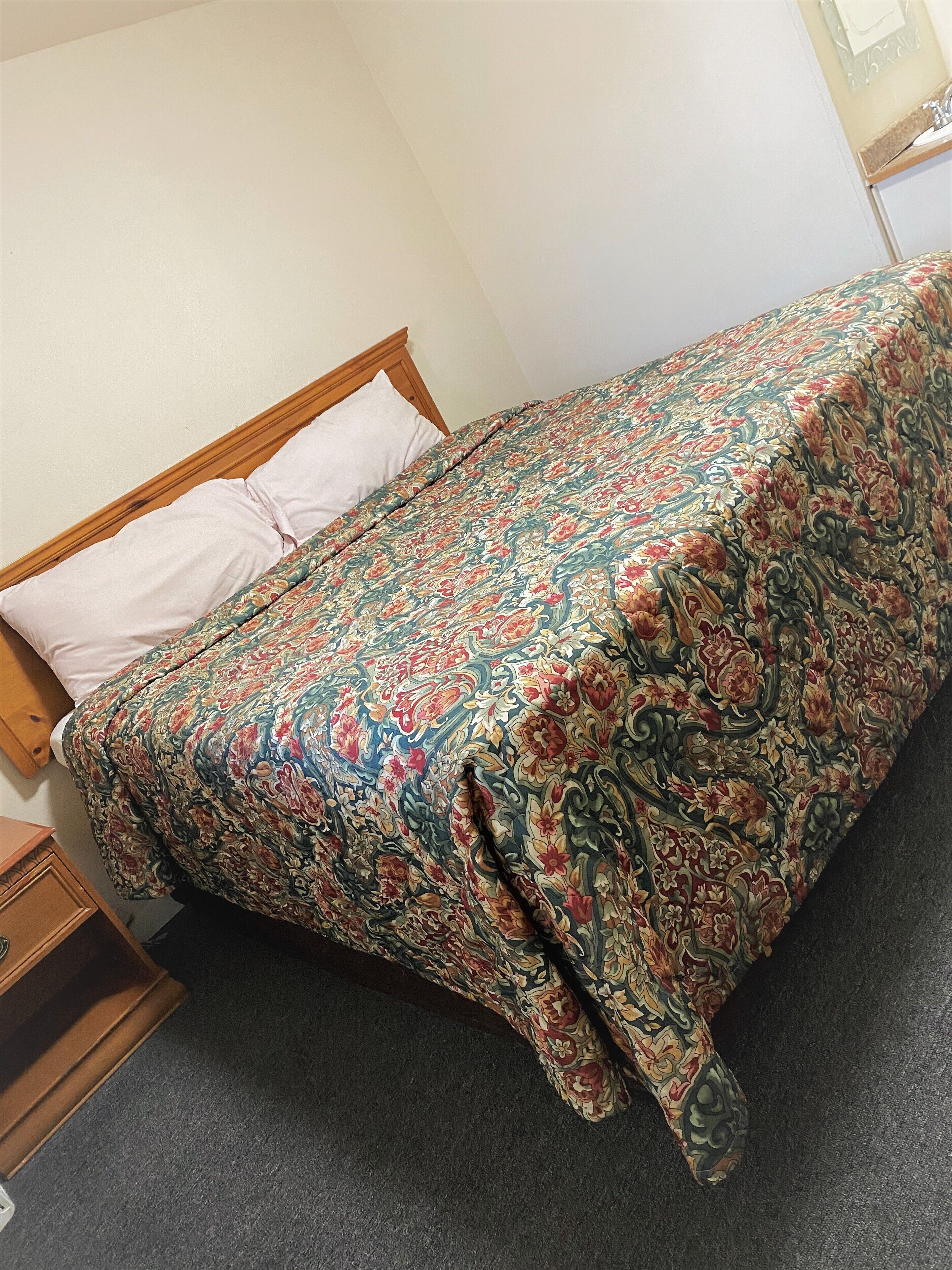 Un lit avec une couvre-lit à motifs floraux, une tête de lit en bois et un simple oreiller blanc.