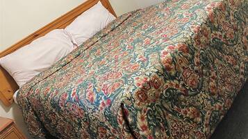 Un lit avec une couvre-lit à motifs floraux, une tête de lit en bois et un simple oreiller blanc.