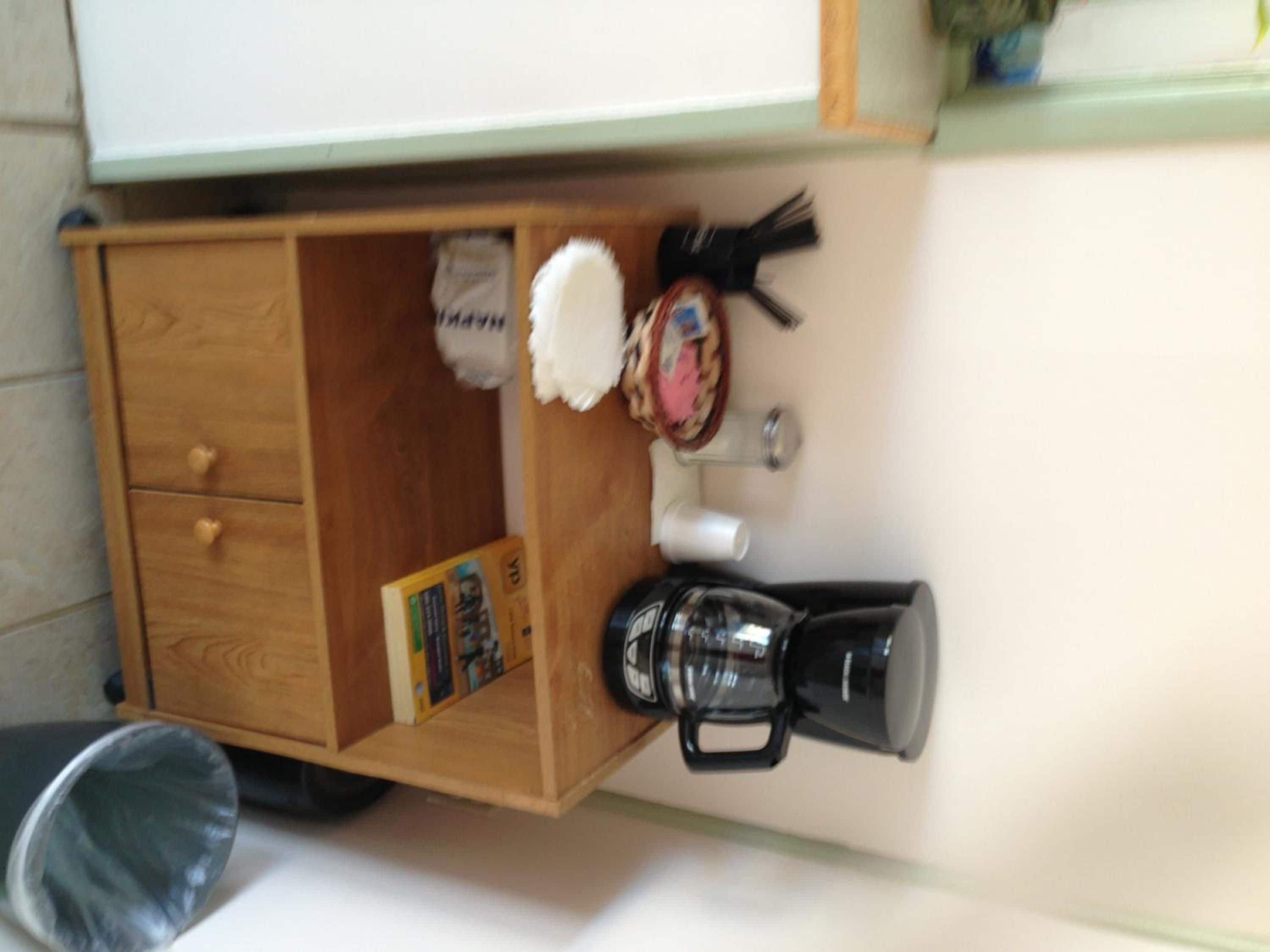 Un mueble de madera con una cafetera, un objeto blanco y esponjoso, y un detalle pequeño en la pared.