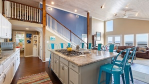 A spacious kitchen with a large island, blue chairs, and a staircase leading to an upper level. - Beachfront Home Perfect For Family Vacations (Galveston)