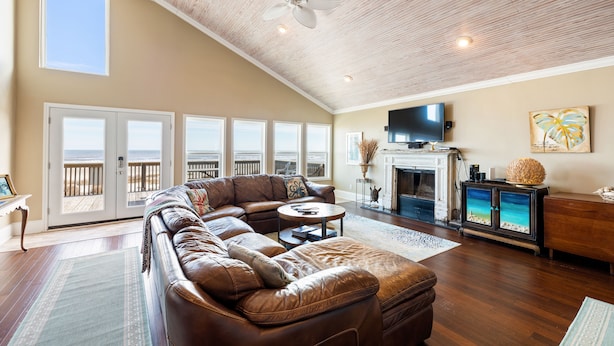 A spacious living room with a large leather sectional sofa, a fireplace, a television, and a view of the ocean through large windows. - Beachfront Home Perfect For Family Vacations (Galveston)