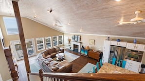 A spacious living room with a large brown leather sofa, a wooden ceiling, and a kitchen area with white cabinets and stainless steel appliances. - Beachfront Home Perfect For Family Vacations (Galveston)