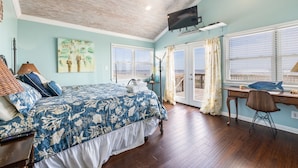 A bedroom with a bed, a desk, and a TV. There is a balcony with a view. - Beachfront Home Perfect For Family Vacations (Galveston)