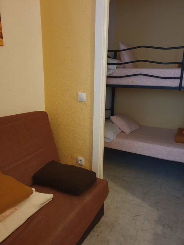A room with a brown sofa, a white wall with a light switch, and a bunk bed with patterned bedding. - Hostal Plaza Luna (Madrid)