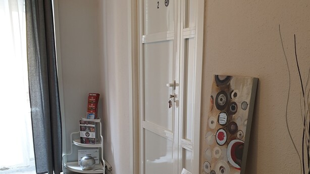 Un pasillo con una puerta blanca, una estantería con objetos y un cuadro en la pared.