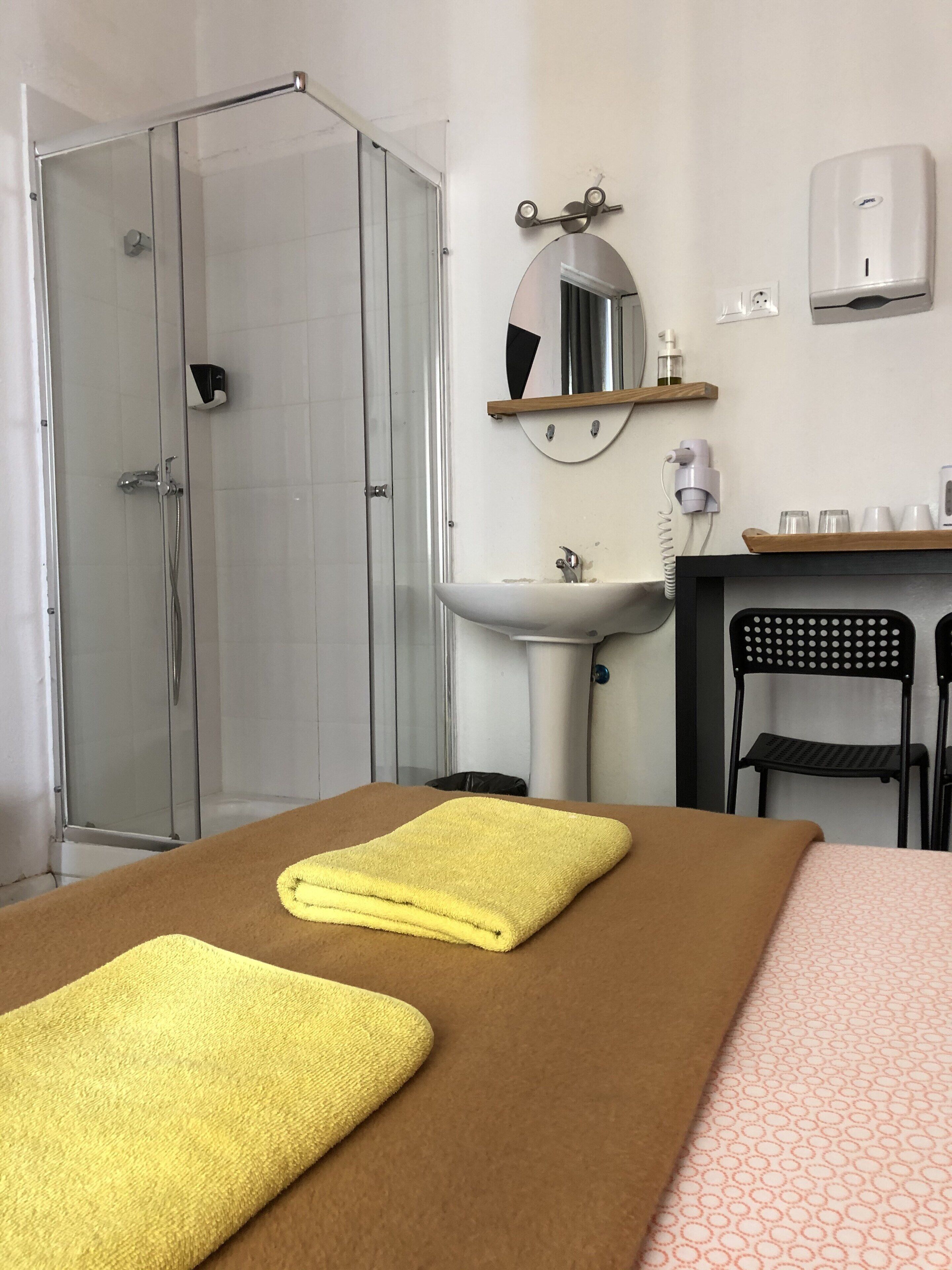 Quarto de hotel com chuveiro, pia, espelho e mesa de massagem com toalhas.