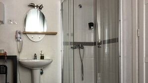 Habitación de hotel con una cama, cabina de ducha acristalada, lavabo y espejo sobre el lavabo.