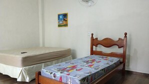 Et soveværelse med en træseng, madras, et lille natbord og en vægmonteret ventilator.