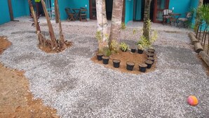 En gårdsplads med grusbelægning, flere krukker med planter og et par stole.