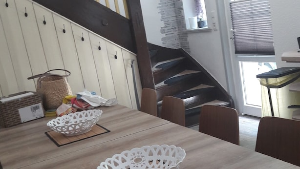 Un coin repas avec une table en bois, deux bols décoratifs blancs et un escalier en arrière-plan.