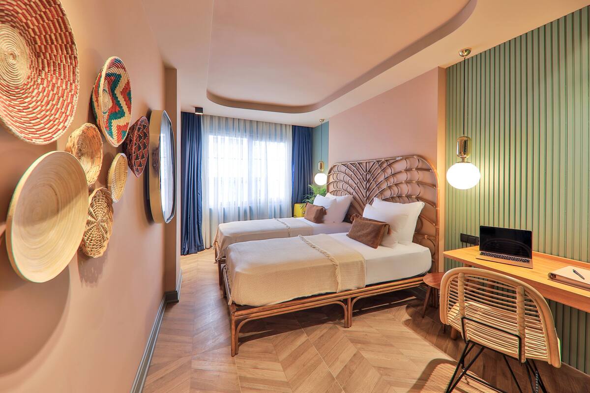 Habitación de hotel con dos camas, un escritorio, una computadora portátil y cestas tejidas en la pared.