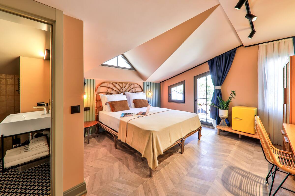 Un dormitorio con una cama, un escritorio, una silla, un ventanal y un baño con lavamanos.