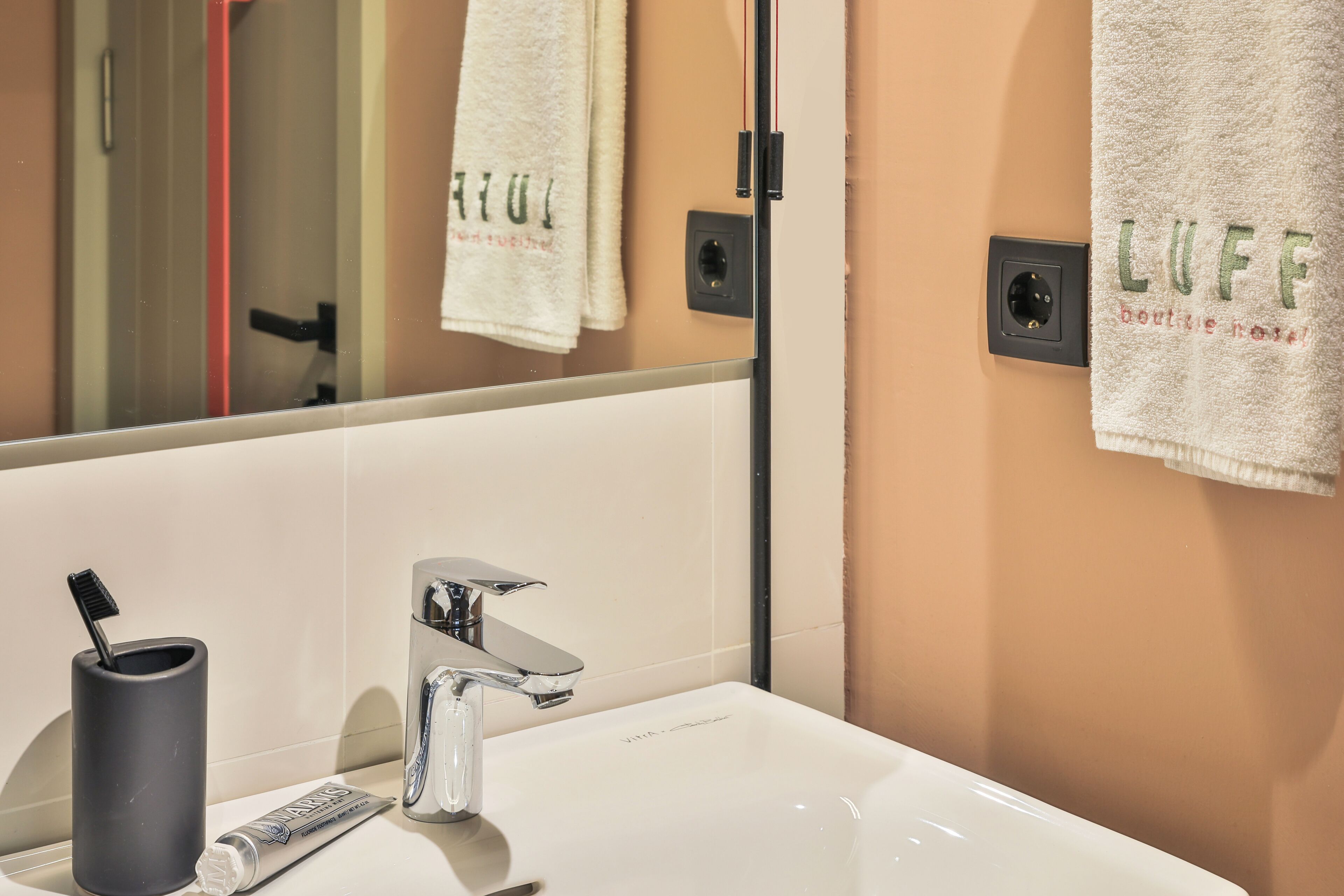 A bathroom with a white sink, a mirror, and two towels hanging on the wall.