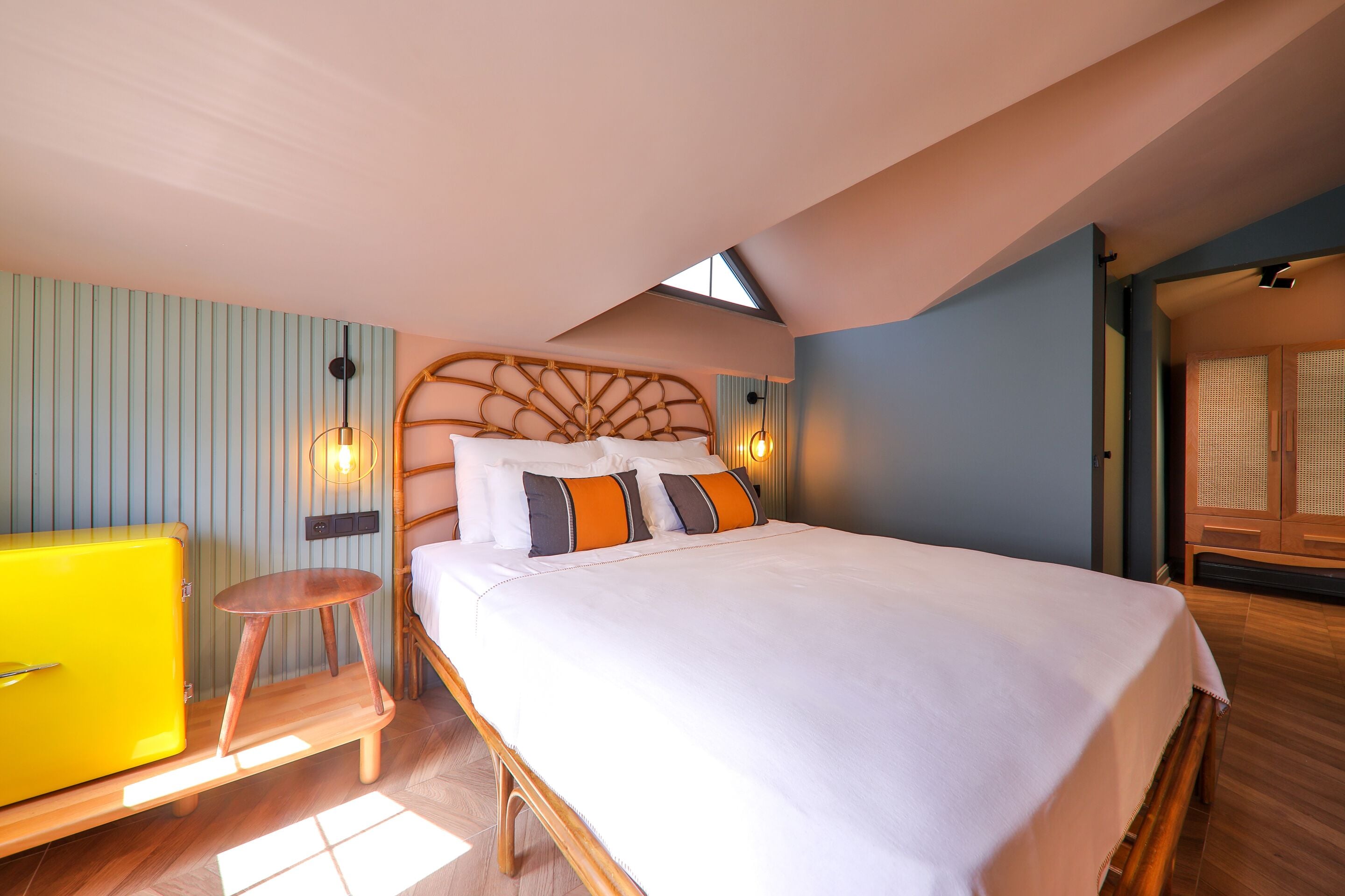 Un dormitorio con una cama, una mesita de noche de madera, un aparador amarillo y un tragaluz.