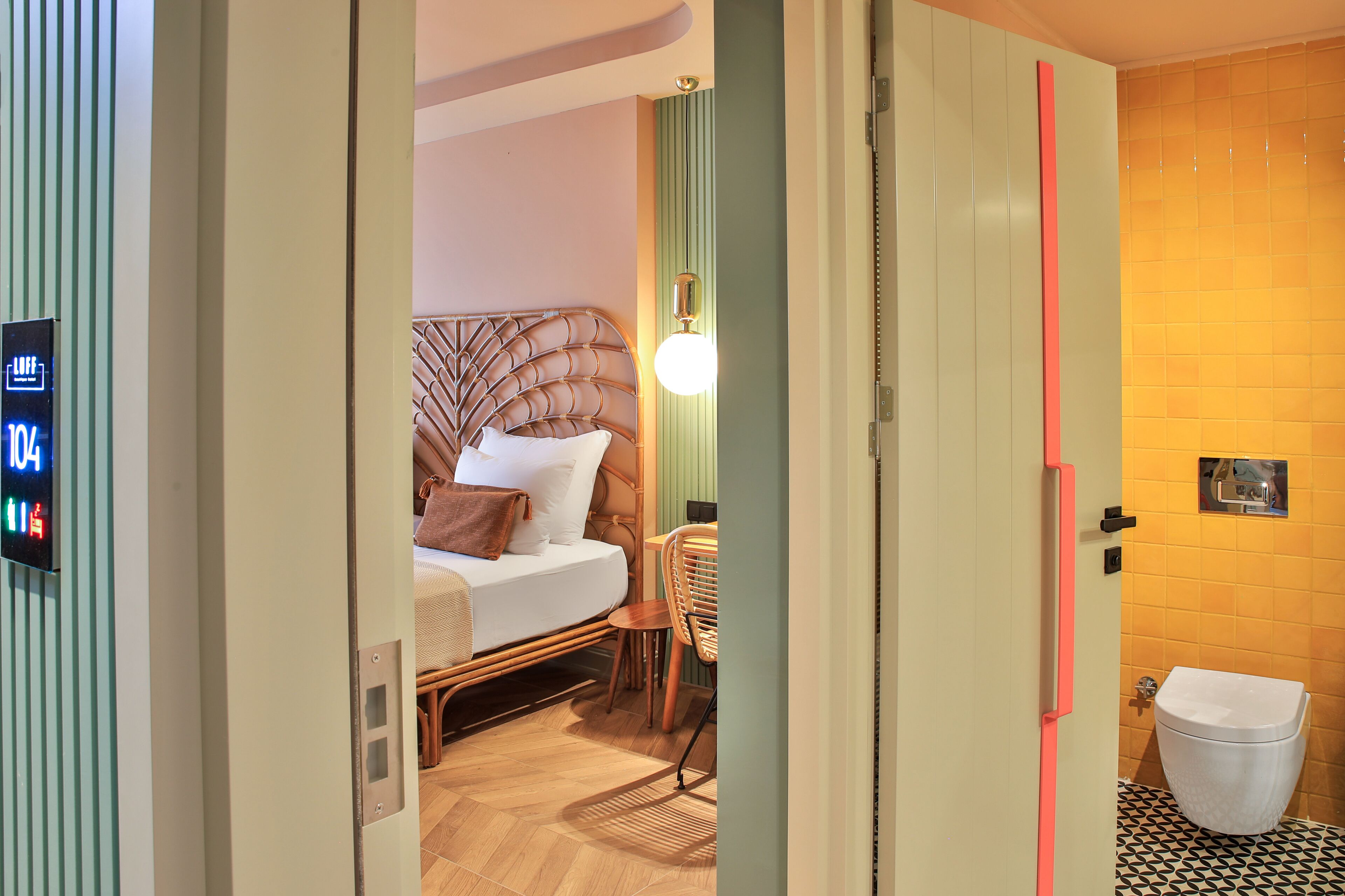 A hotel room with a bed, bedside table, lamp, and a view of the bathroom.