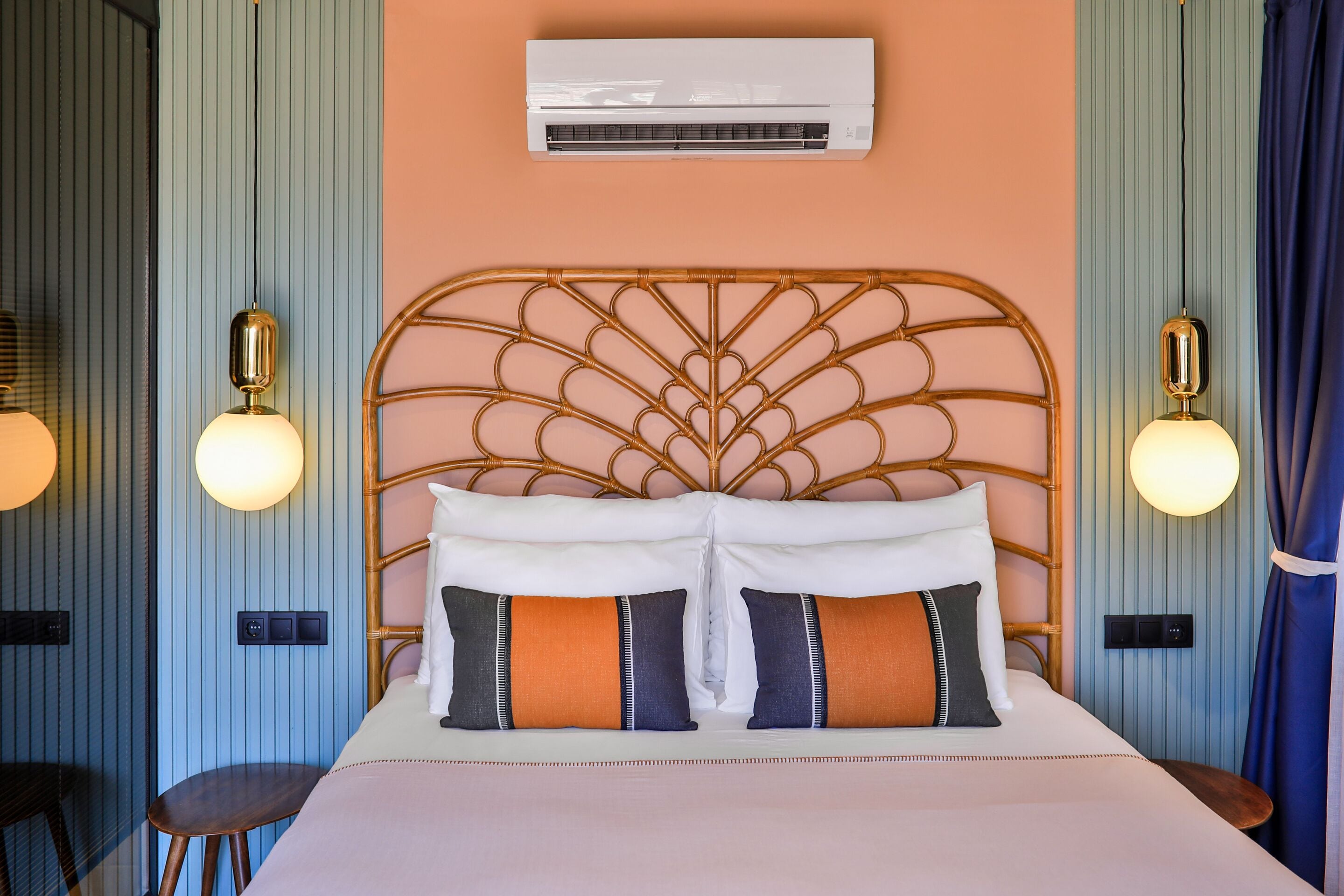 A hotel room with a bed, a wall-mounted air conditioner, and two wall sconces.