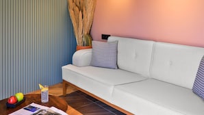 Una sala de estar moderna con un sofá de color gris claro, una mesa de centro de madera con una revista, un vaso de agua y un cuenco de fruta.