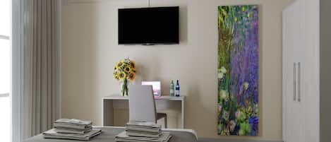 Une chambre d’hôtel moderne équipée d’un lit, d’un bureau, d’une télévision et d’un grand tableau représentant des motifs floraux.