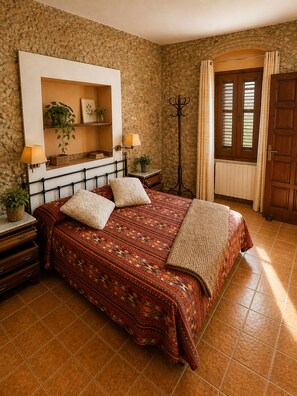 A bedroom with a bed, a nightstand, a lamp, a wall-mounted shelf with decorative items, and a door with a window.
