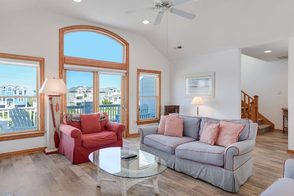 A spacious living room with large windows, a ceiling fan, and a staircase leading to another level.