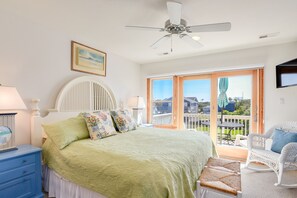 A bedroom with a bed, a nightstand, a dresser, a ceiling fan, and a balcony with a view of the outside.