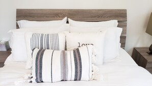 Un lit bien fait, avec une literie blanche, une tête de lit en bois et plusieurs coussins décoratifs.