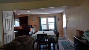 Un comedor con una mesa dispuesta para cuatro, una cocina al fondo y una puerta que da a otra habitación.