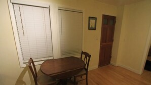 Un comedor con una mesa y sillas de madera, una puerta y un ventanal con persianas.
