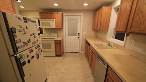 Una cocina compacta con armarios de madera, un refrigerador blanco, un microondas, una estufa y un lavavajillas.