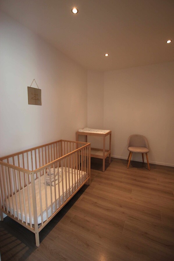 A room with a wooden crib, a small table, and a chair.