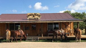 Un bâtiment en bois avec une enseigne indiquant « KIRK'S CREEK SALOON » et un toit en métal. On peut voir trois chevaux devant le bâtiment.