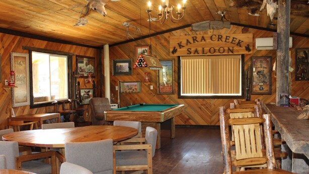 Ein Holzinterieur mit einem Billardtisch, Billardstöcken und einem Schild mit der Aufschrift 'Kara Creek Saloon'.
