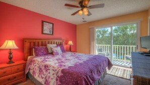 A bedroom with a bed, two bedside lamps, a ceiling fan, a window with a view, and a TV on a dresser. - Emerald_island_8515n (Kissimmee)