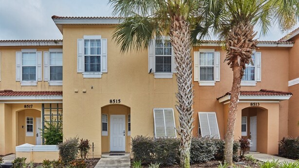 A two-story building with a yellow facade, numbered 8515, featuring a central entrance with a white door, flanked by windows with white shutters. - Emerald_island_8515n (Kissimmee)
