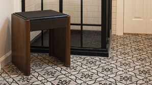A shower enclosure with a glass door, a small wooden stool, and a tiled floor.