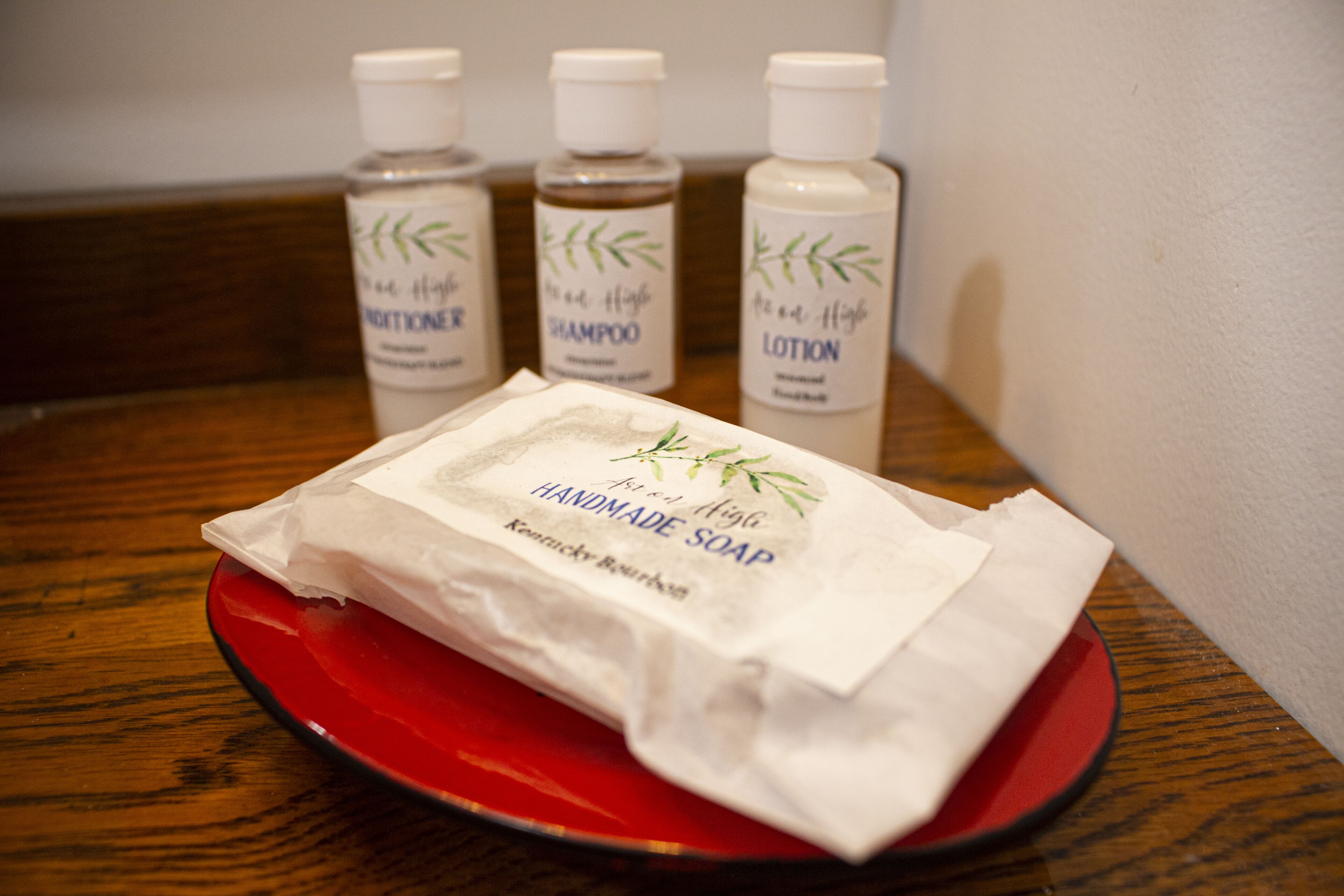 A red tray with a package of handmade soap and three bottles of hair care products in the background.