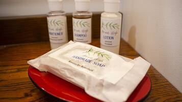 A red tray with a package of handmade soap and three bottles of hair care products in the background.