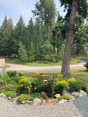 Stroll along the gravel path to a serene seating area surrounded by lush plants and a majestic tree.