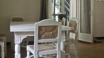 Een eetruimte met een witte tafel en stoelen, een kroonluchter en een schilderij aan de muur.
