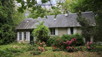 Een klassiek huis met schuine dak, omgeven door weelderige begroeiing en bloeiende planten.