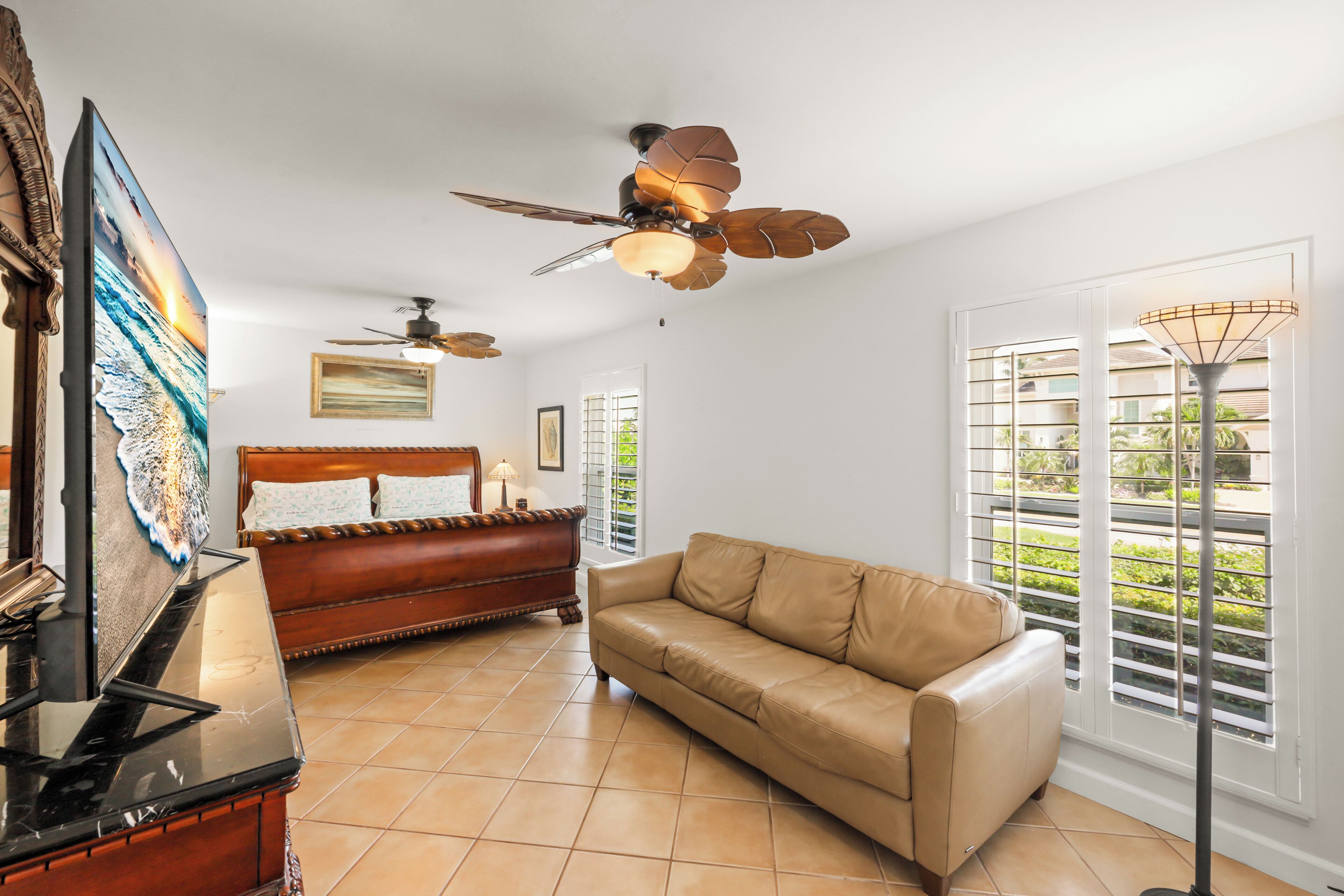A spacious living room with a large sofa, a wooden coffee table, a ceiling fan, and a large window with blinds.