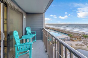 A balcony with turquoise Adirondack chairs, a pool area with lounge chairs, and a view of the beach and ocean. - Direct OCEANFRONT Beautifully Remodel 4th Floor Myrtle Beach Resort (Myrtle Beach)