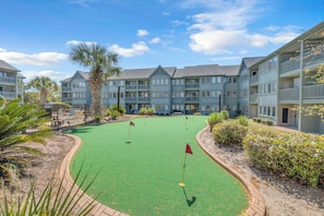 Un campo de golf con un fairway verde, bunkers de arena y un putting green, rodeado de edificios de varios pisos con balcones.