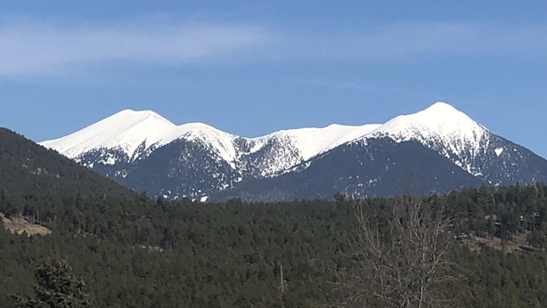 A mountain range with snow-capped peaks and a forested valley.