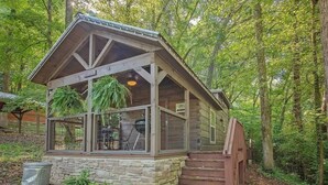 A cabin with a stone foundation, wooden walls, a pitched roof, and a wooden staircase leading to the entrance.