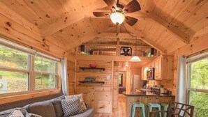A wooden cabin interior with a dining area, kitchen, and a loft bedroom.