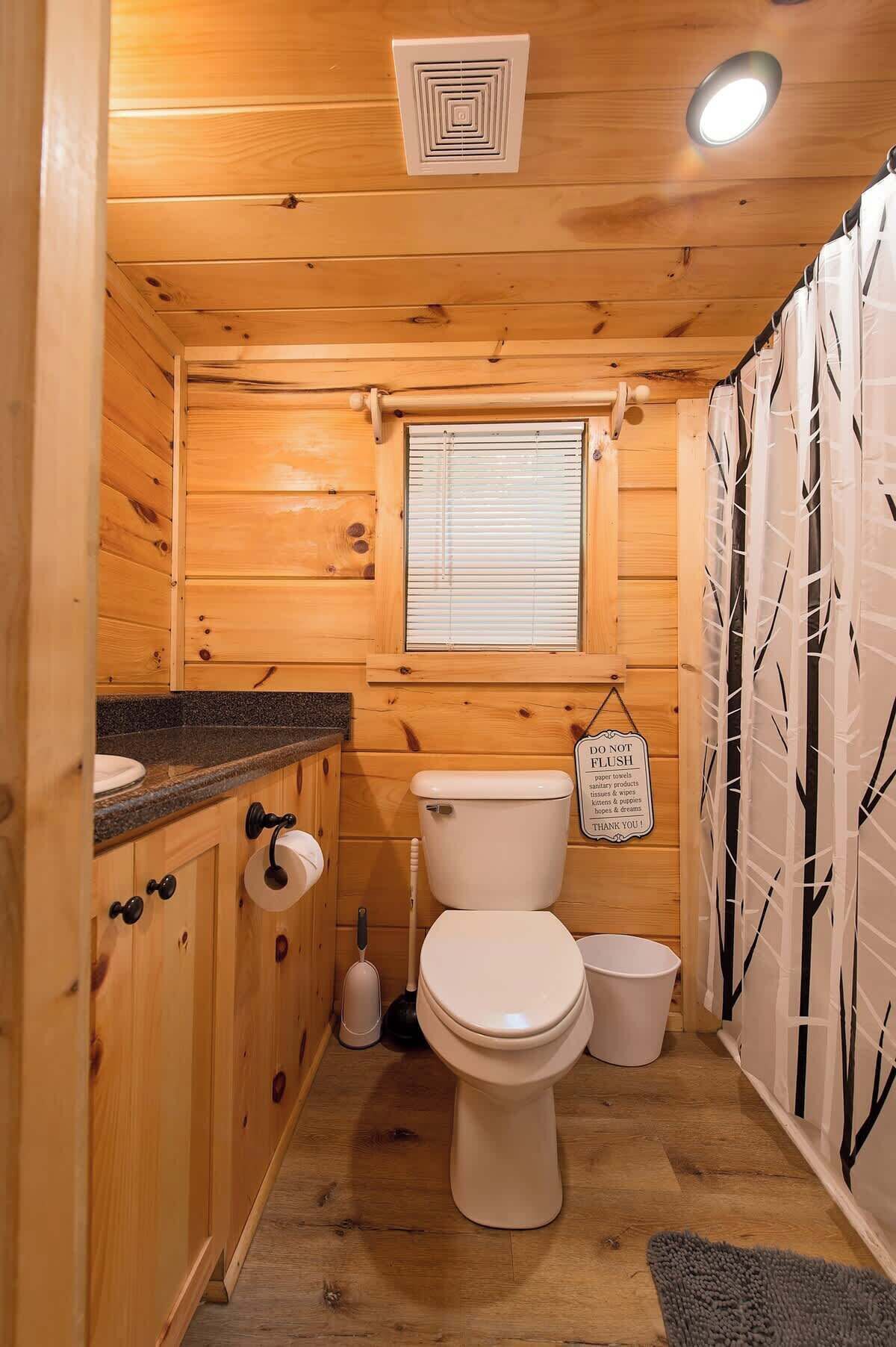 A compact wooden bathroom with a toilet, sink, and window.